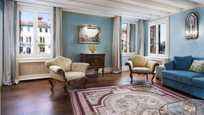 Un salon spacieux avec une grande fenêtre, deux fauteuils, un canapé bleu et un tapis à motifs.