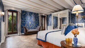 Une chambre dotée d’un grand lit, d’un coin salon et offrant une vue sur la verdure par la fenêtre.