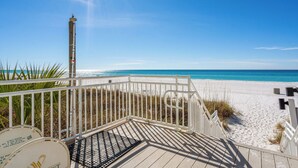 Eine Holzterrasse führt zu einem Sandstrand, der von einem klaren, blauen Himmel überdacht wird.