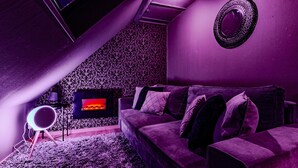 Un salón con decoración morada, un sofá, un papel tapiz estampado y una televisión.