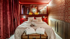 Una camera d'hotel con un letto grande, tende rosse, una testiera in legno e uno specchio fissato alla parete.