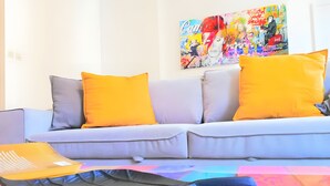 Una sala de estar moderna con un sofá, cojines y un cuadro colorido en la pared.