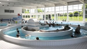 Una amplia piscina interior con varias pistas de natación, una isla central y vistas al exterior a través de grandes ventanales.