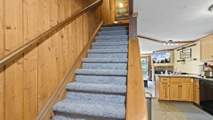 Una escalera de madera con escalones alfombrados que conduce a una zona de cocina con armarios de madera y vistas a un paisaje nevado.