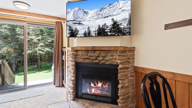 Una chimenea de piedra con un televisor encima, un sillón y una vista de una montaña nevada a través de un ventanal.