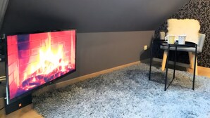 A cozy room with a fireplace, a small table with two cups, a fluffy chair, and a patterned wall.