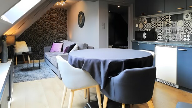 A modern loft bedroom with a skylight, a dining area with a round table, a kitchenette, and a patterned wall.