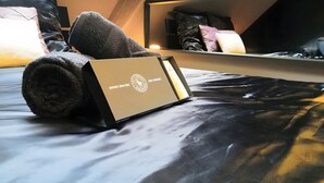 A neatly made bed with a rolled towel and a box on it.