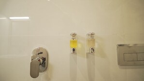 Ett badrum med en kromad kran, tv å behållare för schampo och duschkräm samt en väggmonterad kontrollpanel.