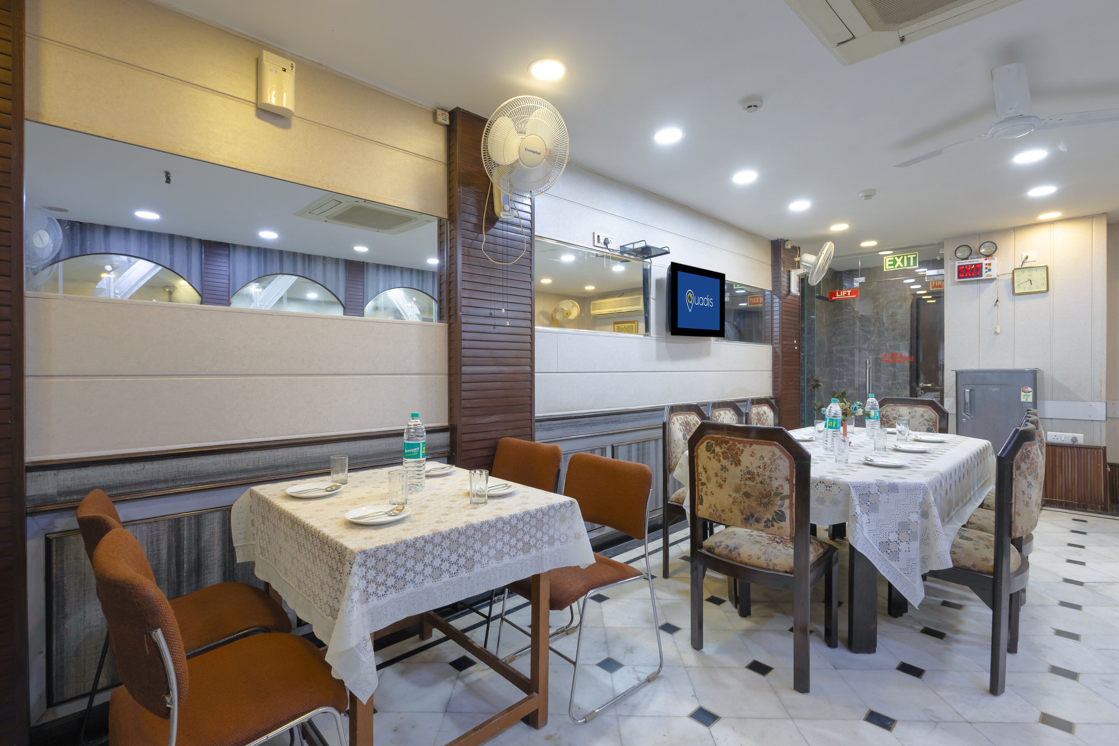 A restaurant with tables set for dining, equipped with chairs, and a television screen displaying the restaurant's name.