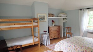 Ein Stockbett, eine Kommode, ein Stuhl, ein kleiner Tisch mit einer Vase und ein Bett mit einer blumigen Tagesdecke.