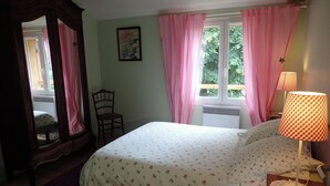 Ein Schlafzimmer mit Bett, Stuhl, Vorhängen am Fenster und einer Lampe.