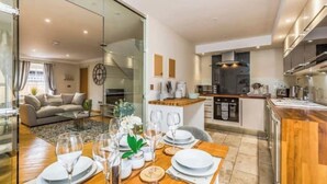 A modern living room with a dining area, a kitchen, and a glass partition.
