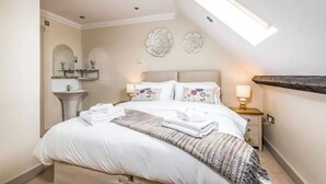 A bedroom with a bed, bedside tables, a nightstand, a wall-mounted mirror, and a skylight.