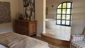 A bedroom with a large bed, a wooden dresser, a painting, and a view of a bathroom with a bathtub. - Escape to Elegance -Wonderful Mas Provencal in the heart of the Alpilles (Saint Etienne du Grés)