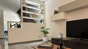 A modern living room with a wooden coffee table, a large flat-screen TV, a potted plant, and a bookshelf.