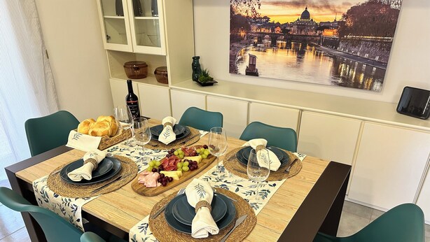 A dining table set with plates, cutlery, and a charcuterie board, surrounded by teal chairs.