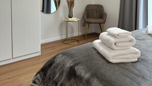 A modern bedroom with a bed, a wardrobe, a round mirror, a small side table, and a chair.