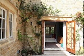 A stone building with a wooden door leading to a room with a bed and a window.