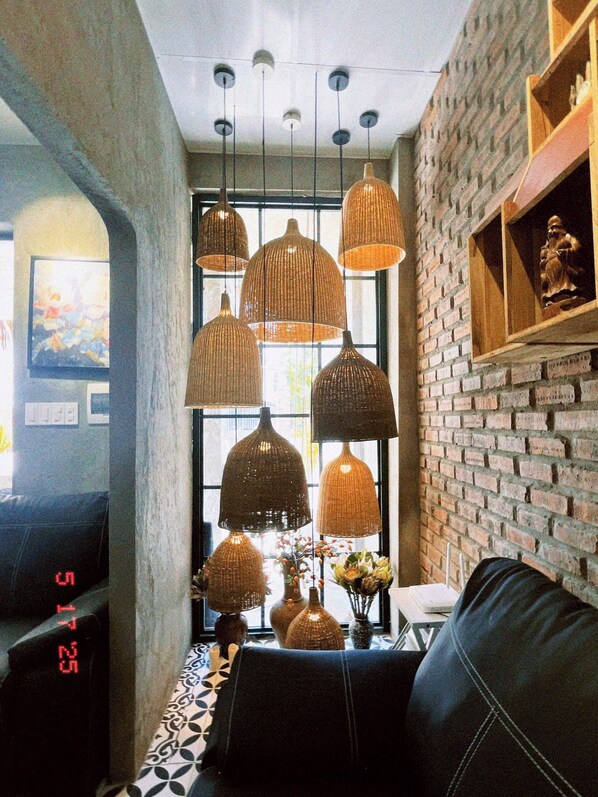 A modern living room with a black leather sofa, a patterned rug, and a brick wall. There are multiple woven pendant lights hanging from the ceiling.