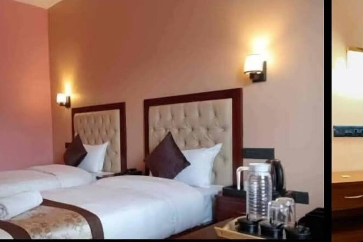 A hotel room with two beds, each with a headboard, a bedside table with a lamp, and a tray with a coffee maker and other items.