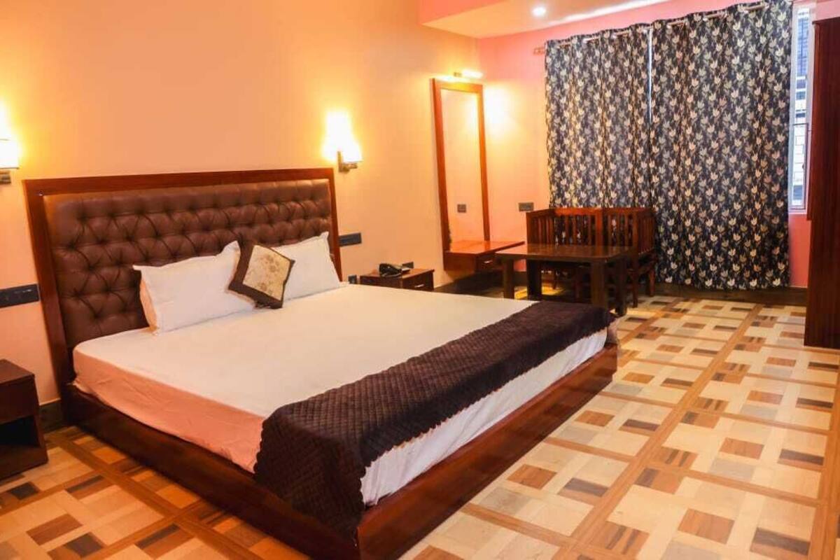 A hotel room with a large bed, a wooden headboard, a bedside table, a desk, and a patterned curtain.