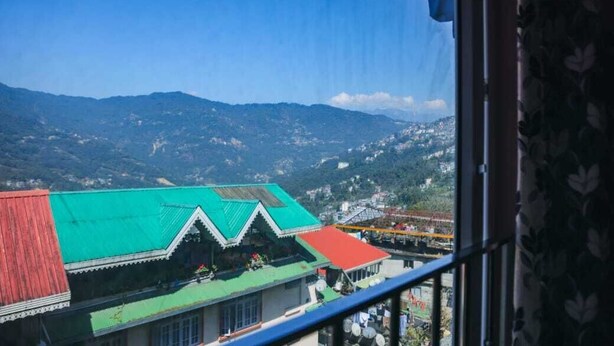A view from a window overlooking a mountainous landscape with a building featuring a green roof and red walls. - Hotel Ronak  By Red Panda (Gangtok)