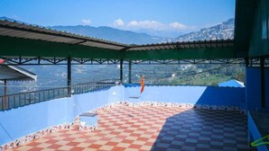 A rooftop terrace with a checkered floor, a view of distant mountains, and a hanging orange object. - Hotel Ronak  By Red Panda (Gangtok)