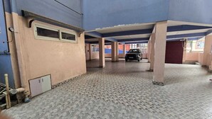 A covered parking area with tiled flooring, pillars, and a car parked in the distance. - Hotel Ronak  By Red Panda (Gangtok)