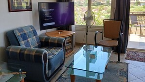 A living room with a sofa, a glass coffee table, a television, and a view of a residential area through large windows.
