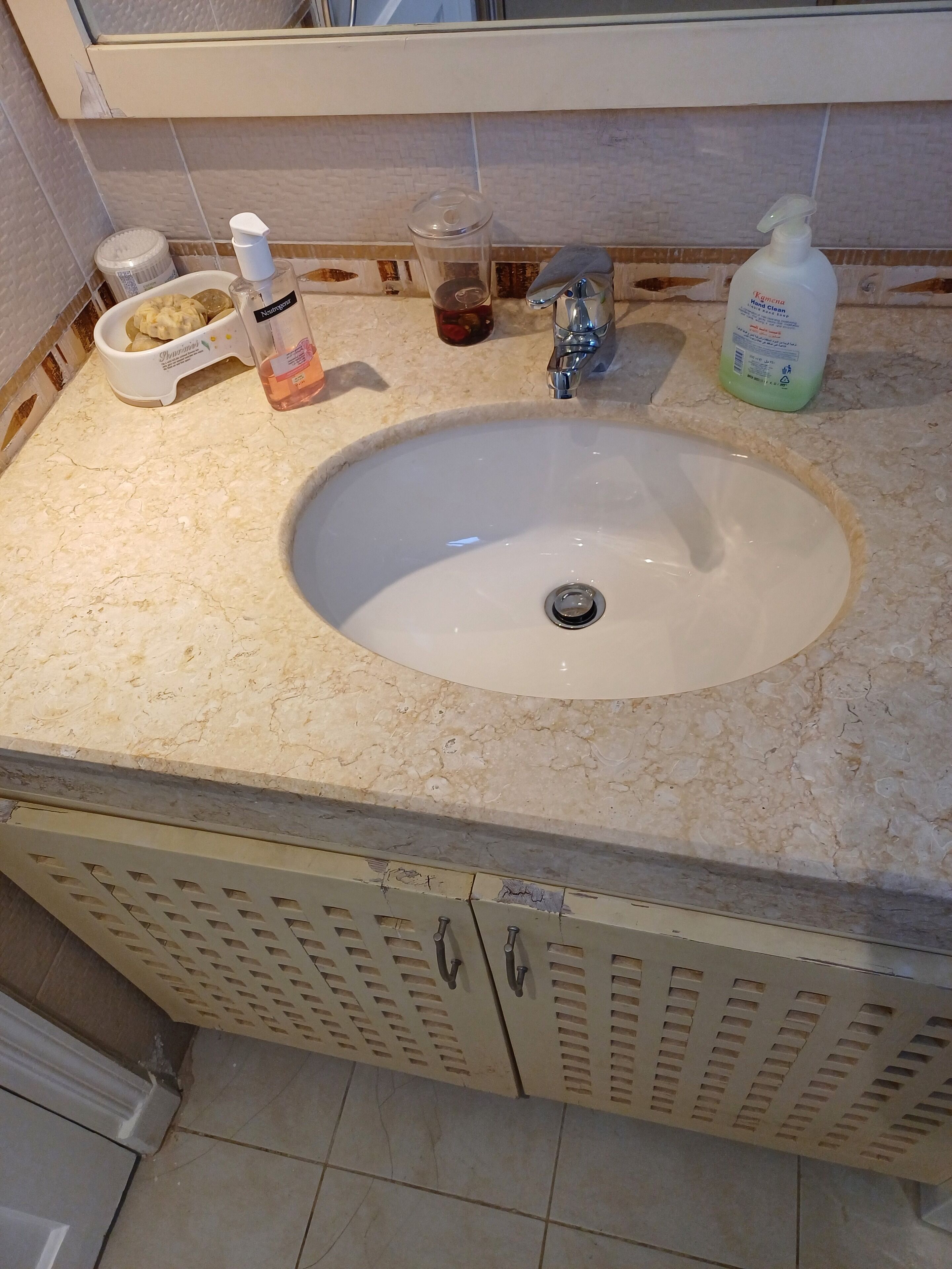 A bathroom sink with a marble countertop, a soap dispenser, a glass of water, and a bottle of hand sanitizer.