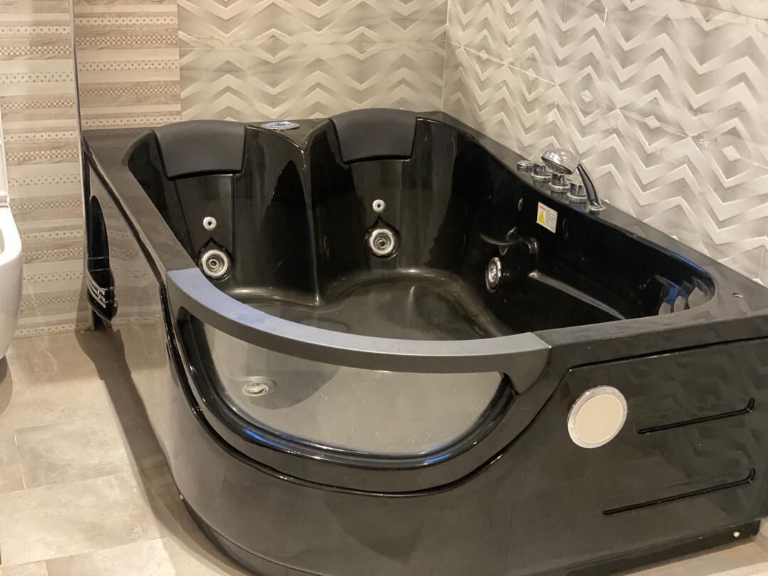 A black jacuzzi tub with a curved design, a control panel, and a glass door.