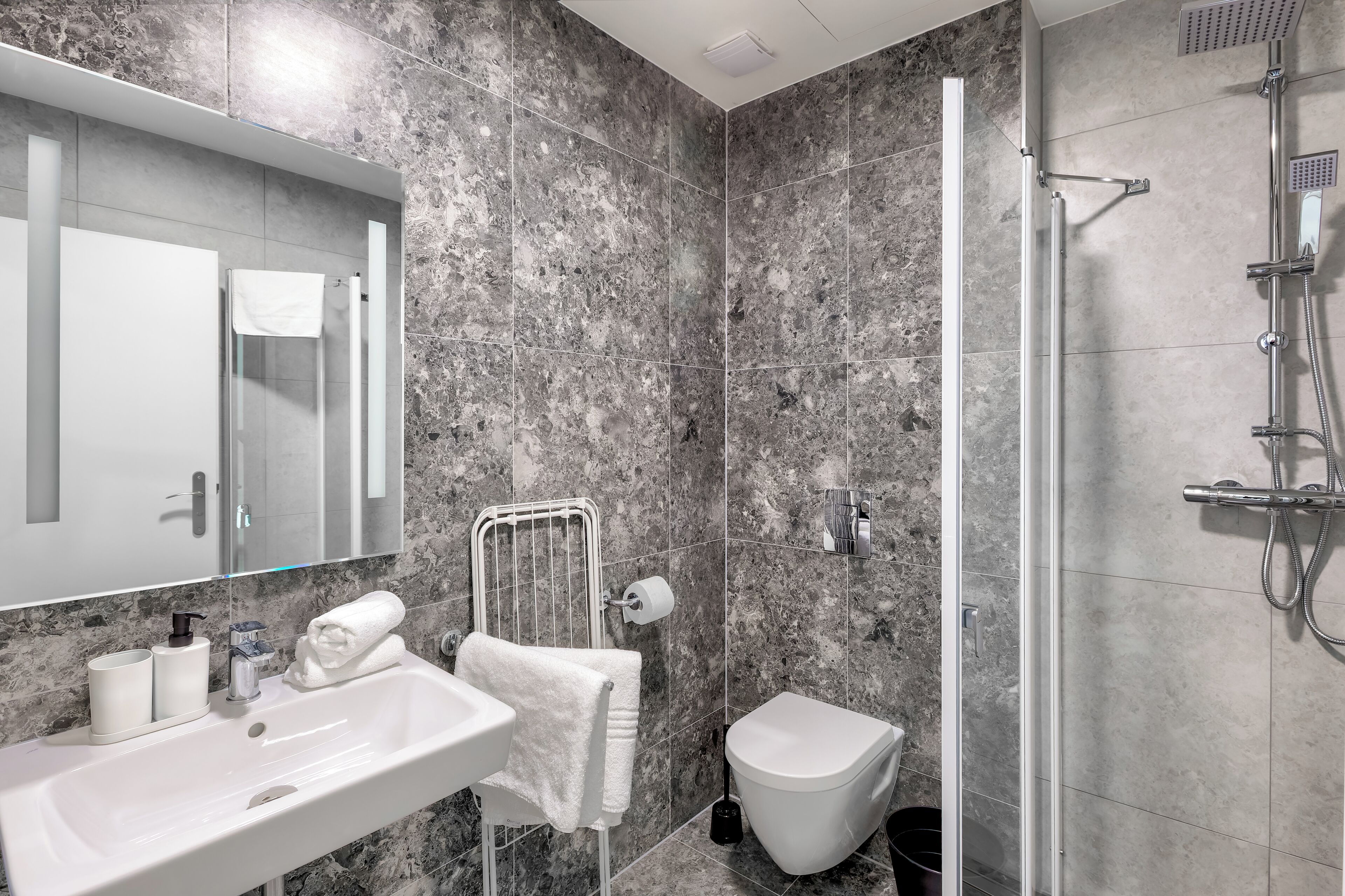 A modern bathroom with a marble backsplash, a white sink, a toilet, and a glass-enclosed shower area.