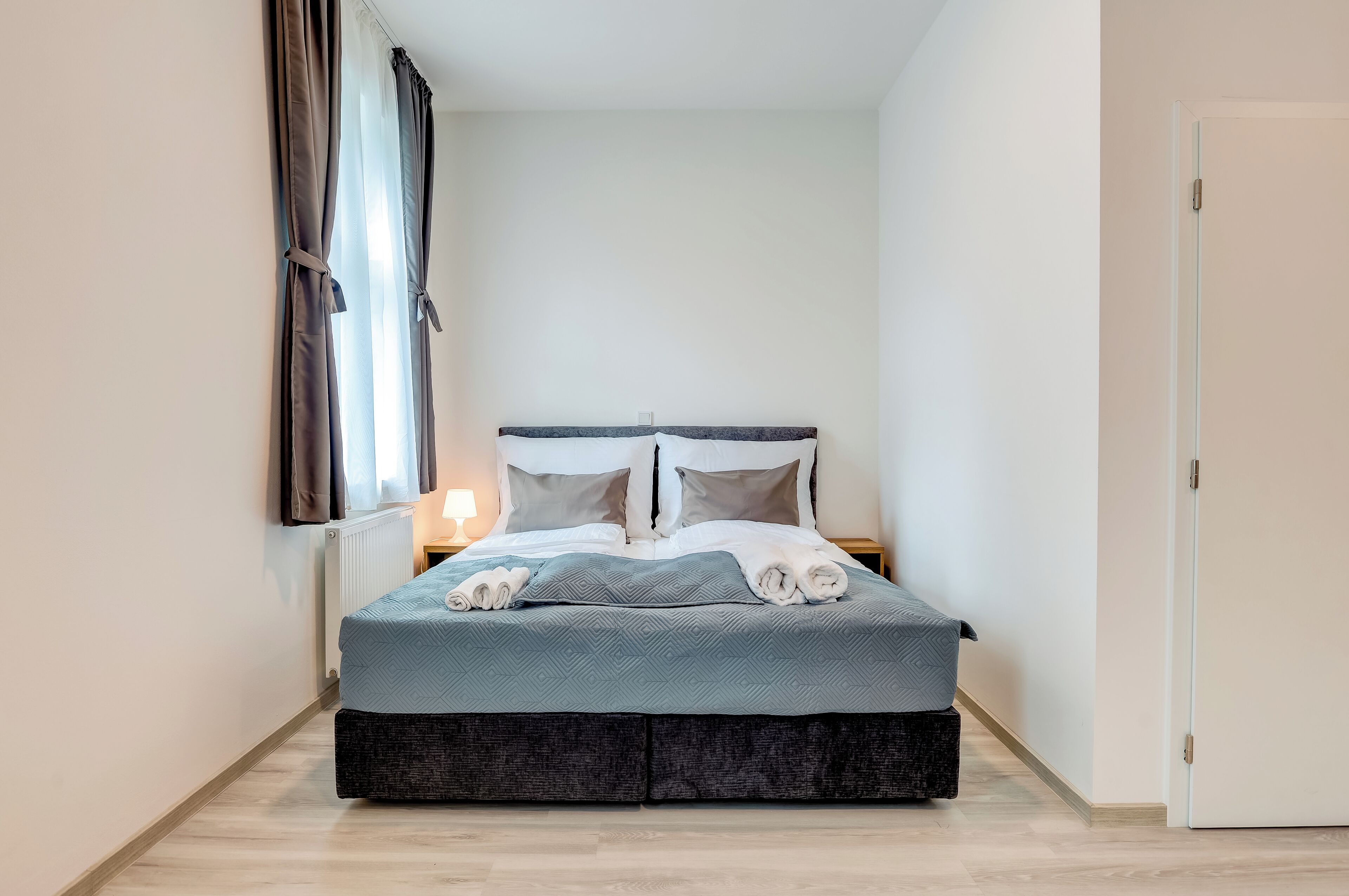Ein ordentlich bezogenes Bett mit einer grau-weißen Bettdecke, einem dunkelgrauen Kopfteil und zwei Kissen.