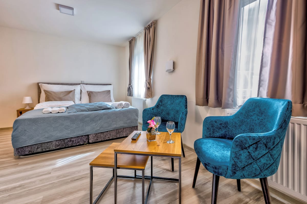 A hotel room with a bed, two chairs, a table, and a window with curtains.