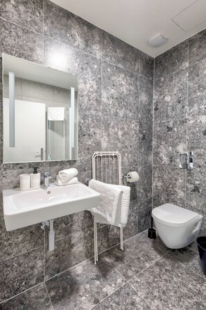 Un baño moderno con un salpicadero de mármol, un espejo grande, un lavabo blanco, un inodoro y un perchero para toallas.