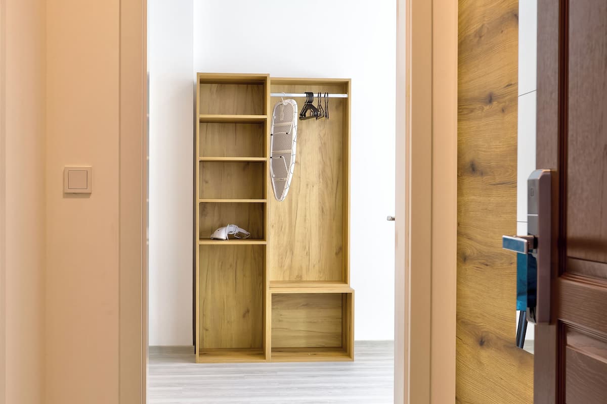 A hallway leading to a wooden closet with shelves and hooks.