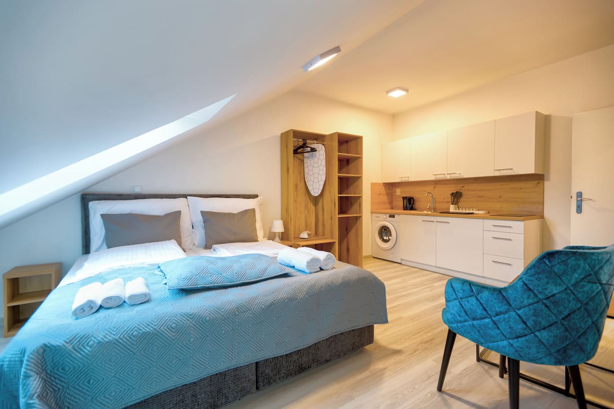 A modern bedroom with a large bed, a washing machine, and a blue chair.