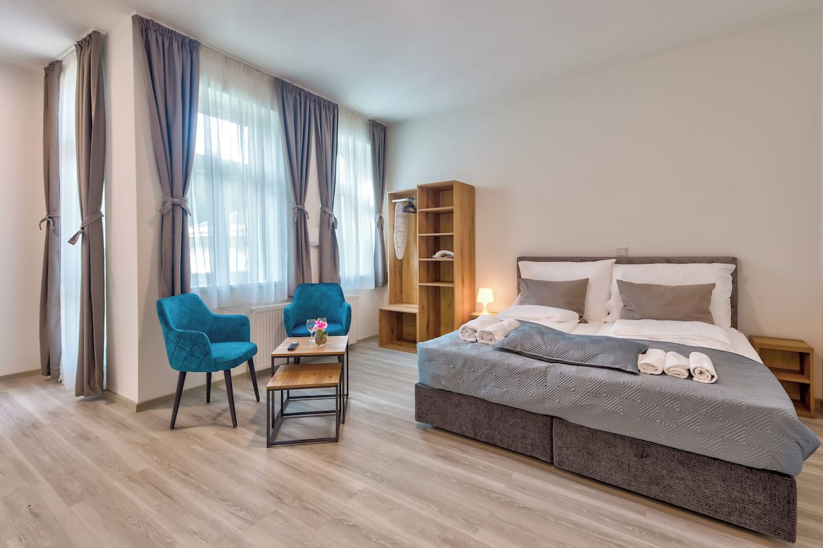 A modern bedroom with a bed, a chair, a small table, a wardrobe, and a window with curtains.