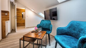 A modern living room with a wooden floor, a wooden wall, a TV mounted on the wall, and two blue velvet sofas.