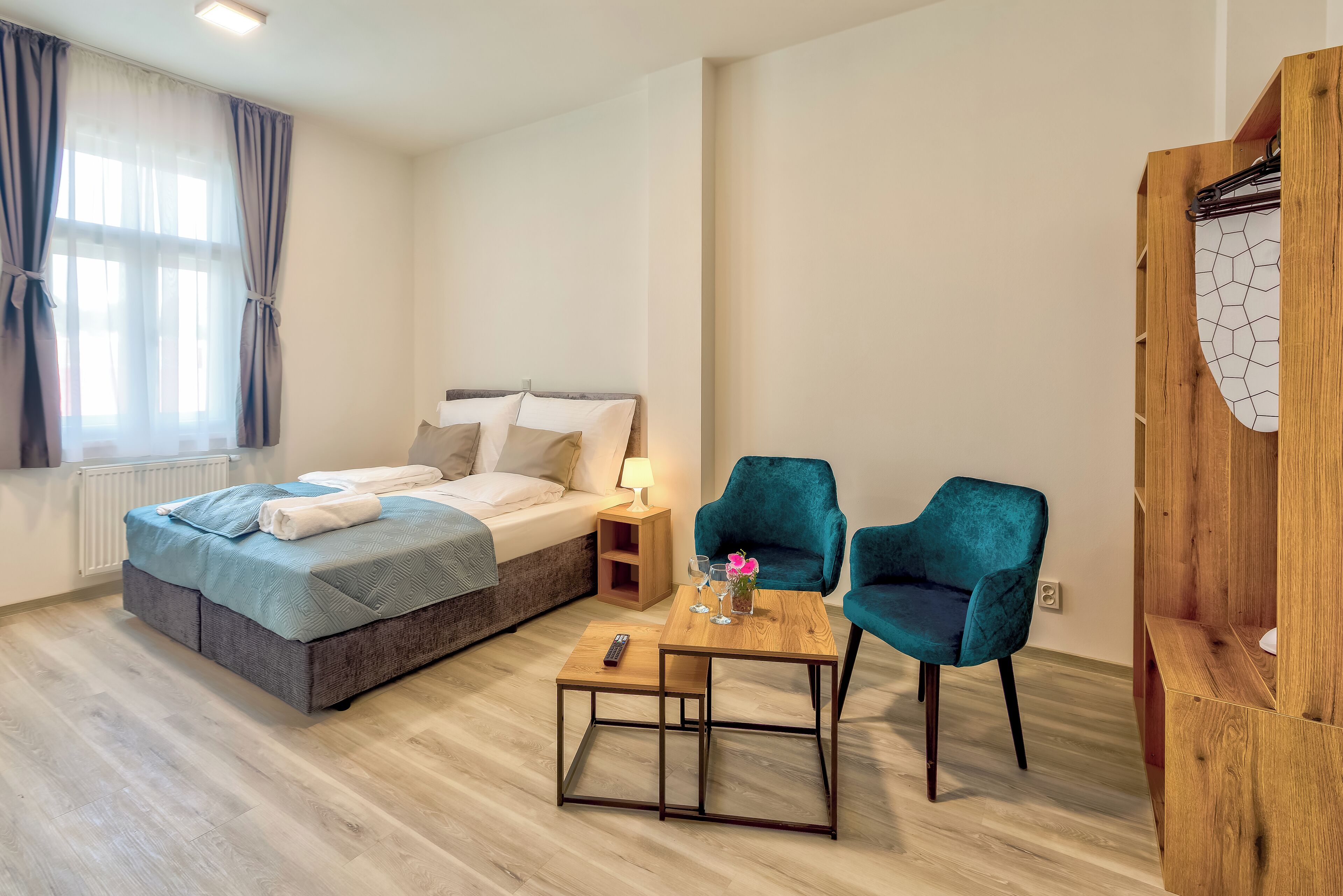 A bedroom with a bed, bedside table, two chairs, a small table, and a wooden wardrobe.