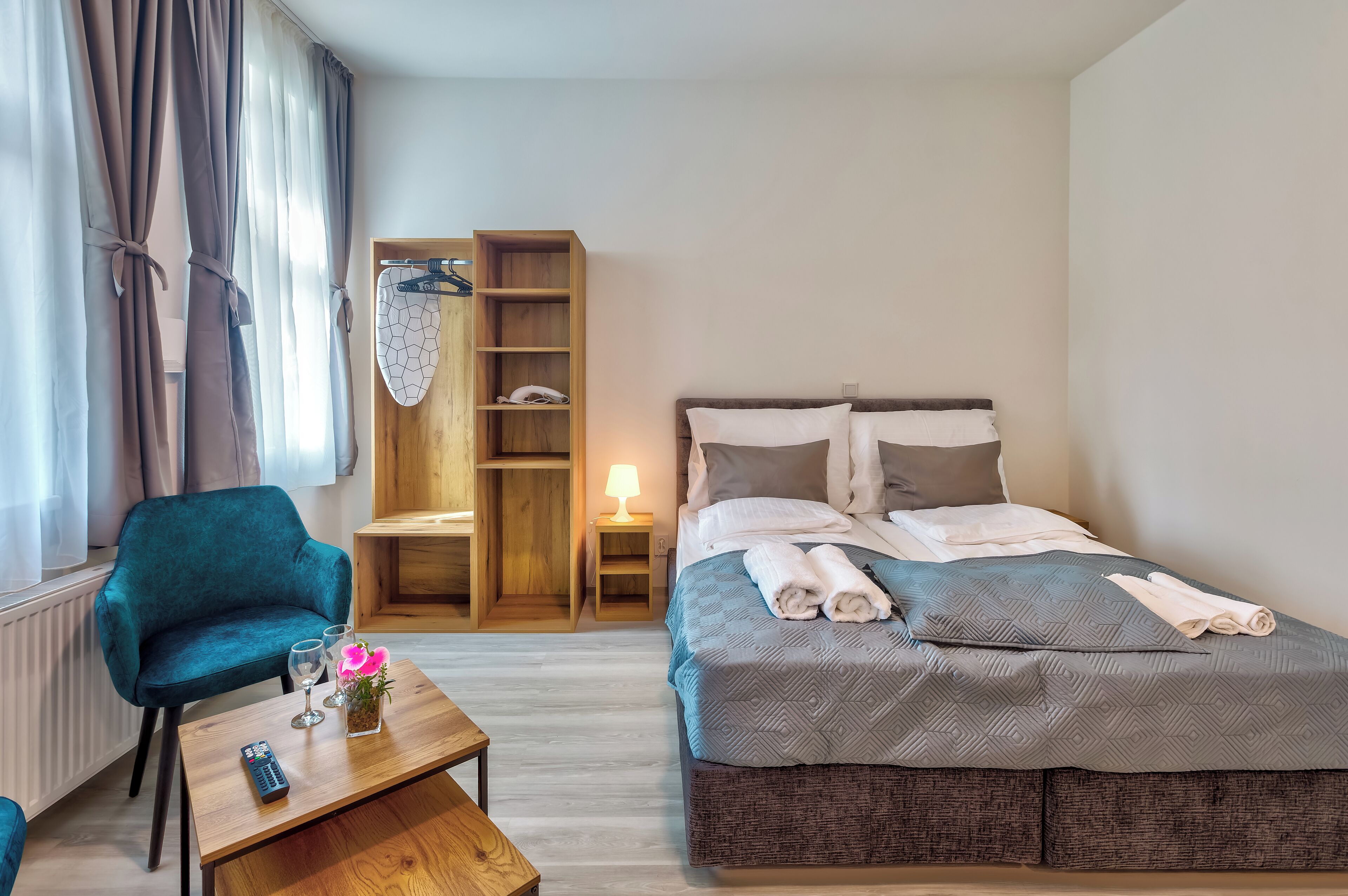 A hotel room with a bed, a chair, a small table, a lamp, and a wardrobe.