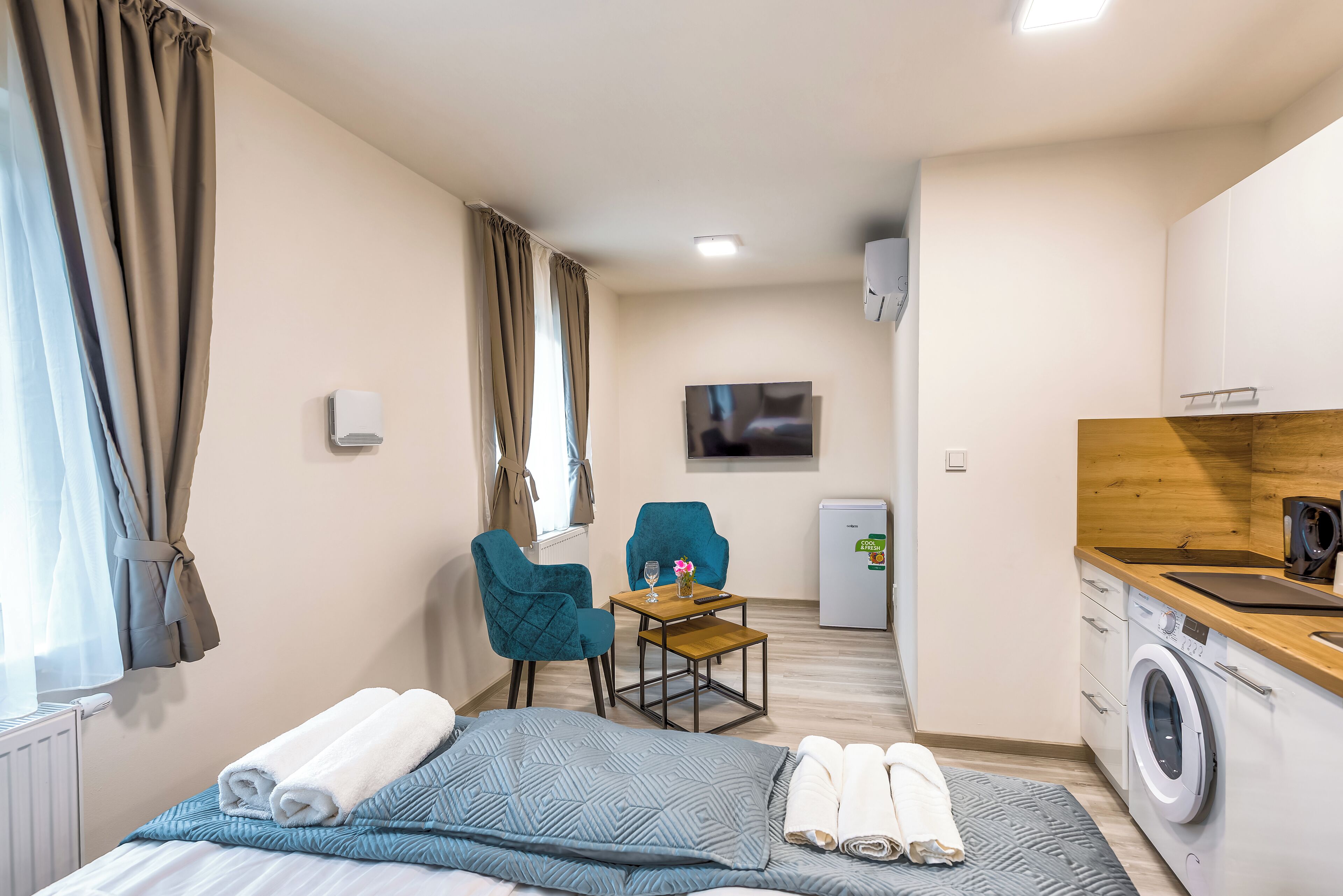 A hotel room with a bed, a desk with a chair, a washing machine, and a television on the wall.