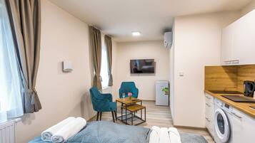 A hotel room with a bed, a desk with a chair, a washing machine, and a television on the wall.
