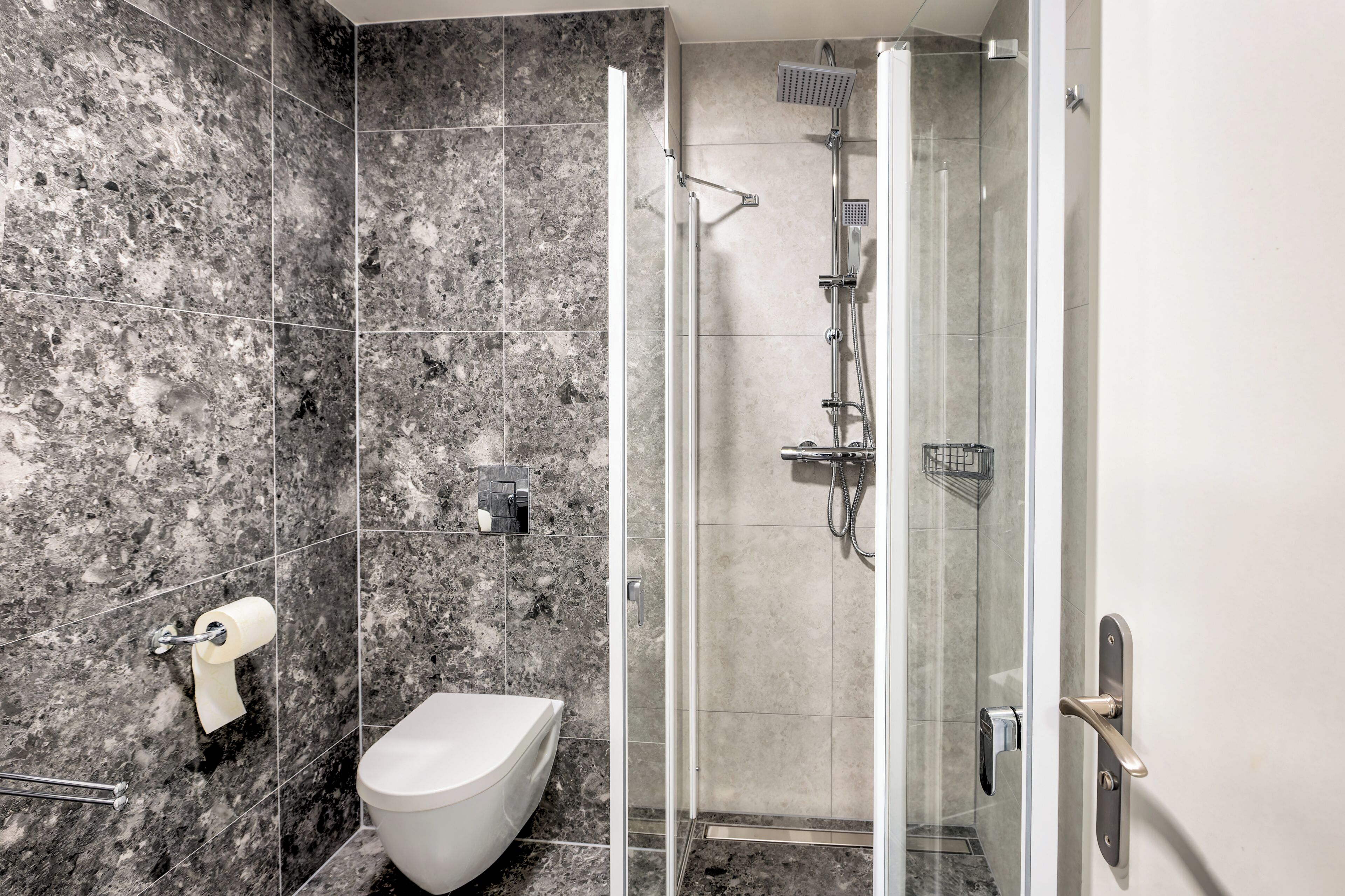 A modern bathroom with a marble floor, a toilet, a shower with a glass door, and a towel rack.