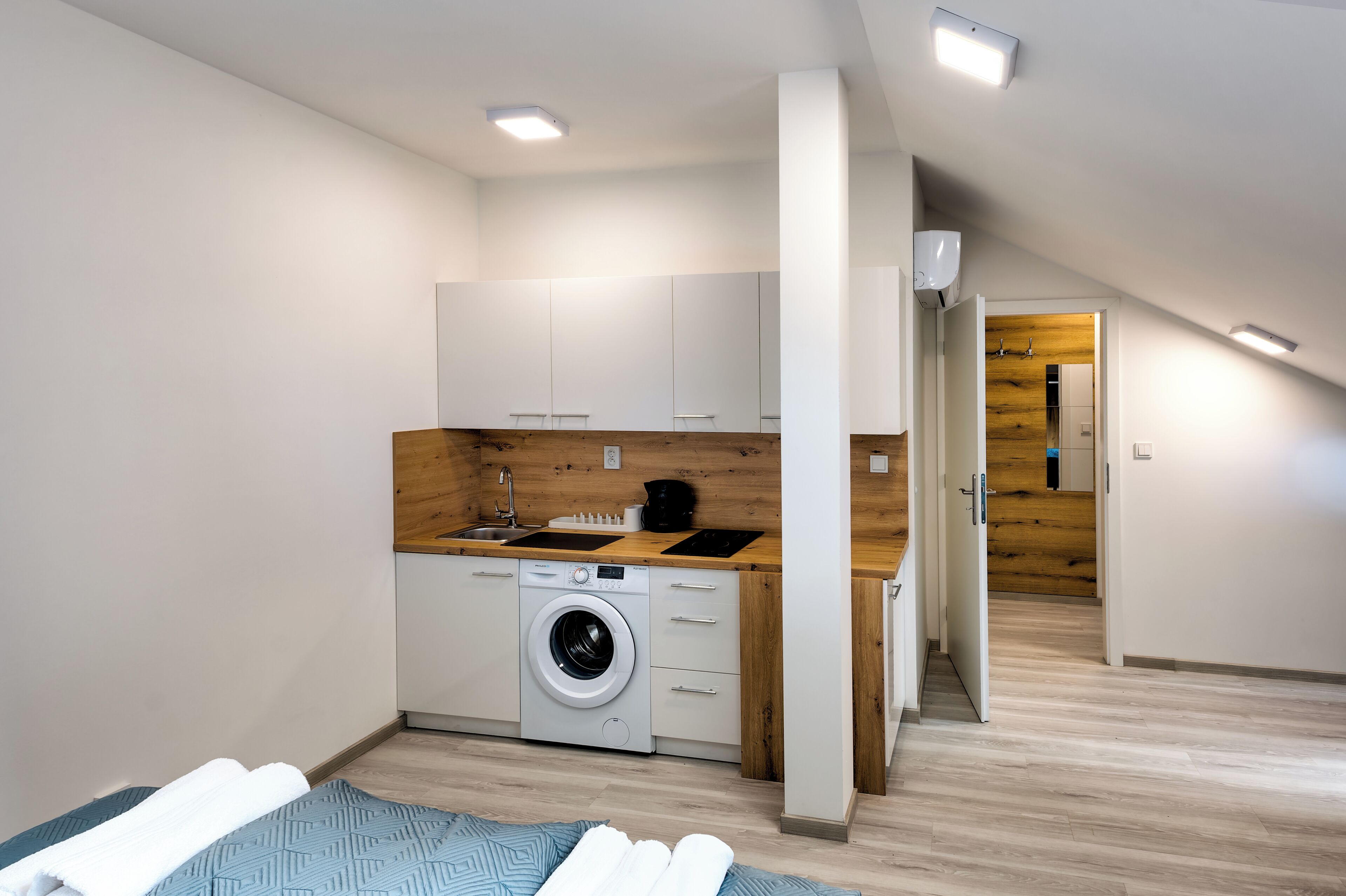 Een compact appartement, modern ingericht, met een kitchenette, een wasmachine en een bed met handdoeken.