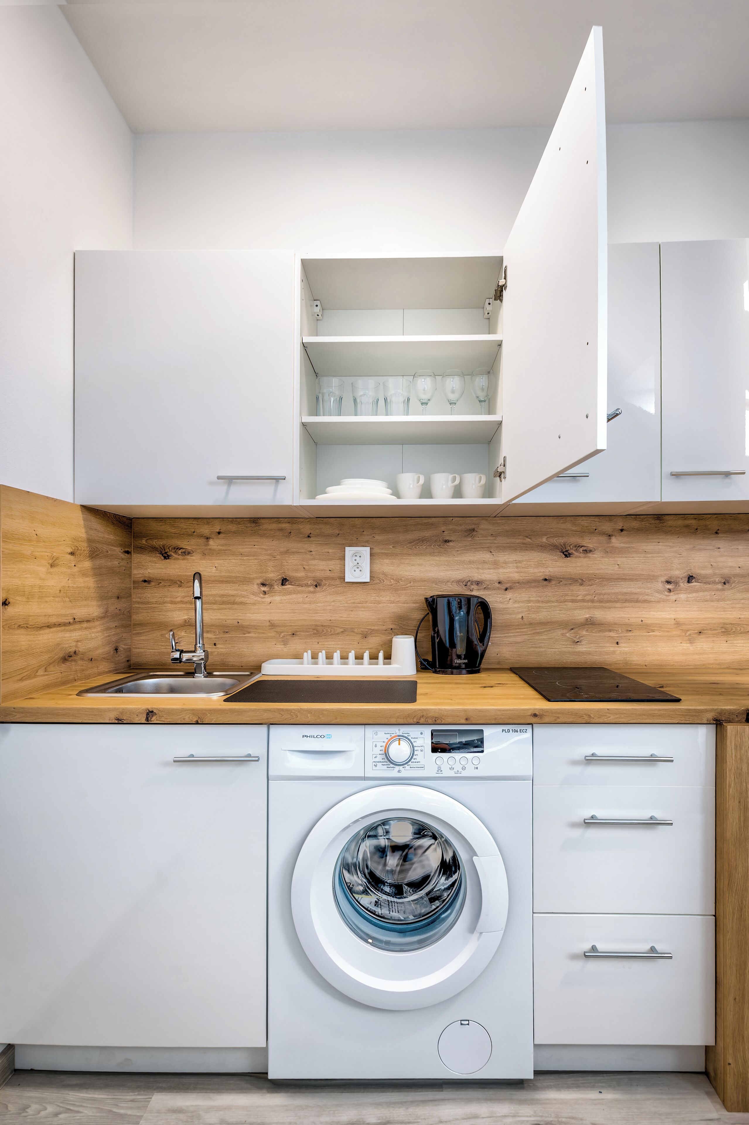 A compact kitchen with a built-in washing machine, wooden countertop, and white cabinetry.