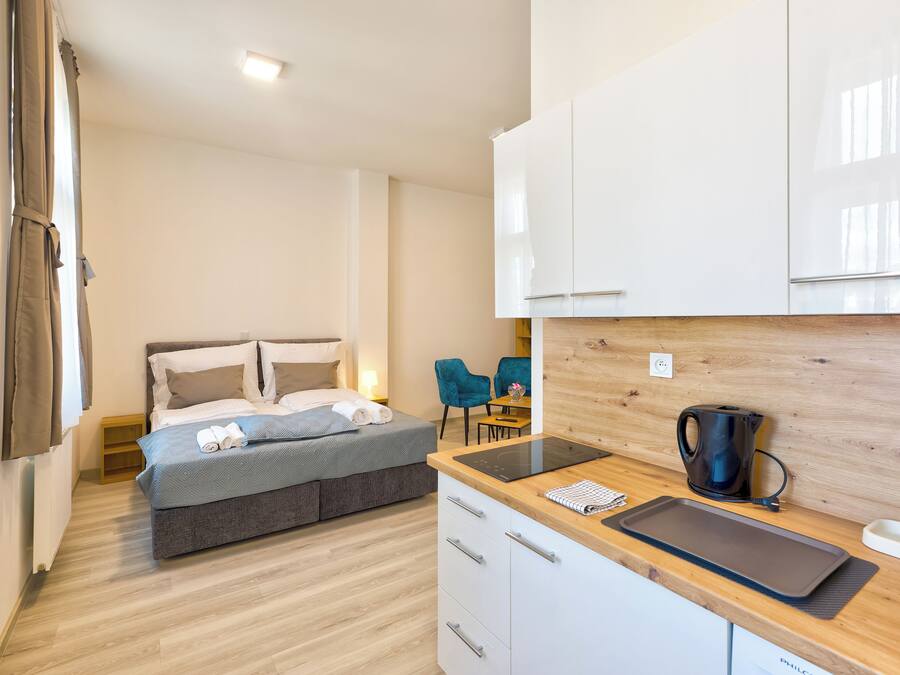 Habitación de hotel moderna con cama, kitchenette, zona de comedor y vistas al exterior.