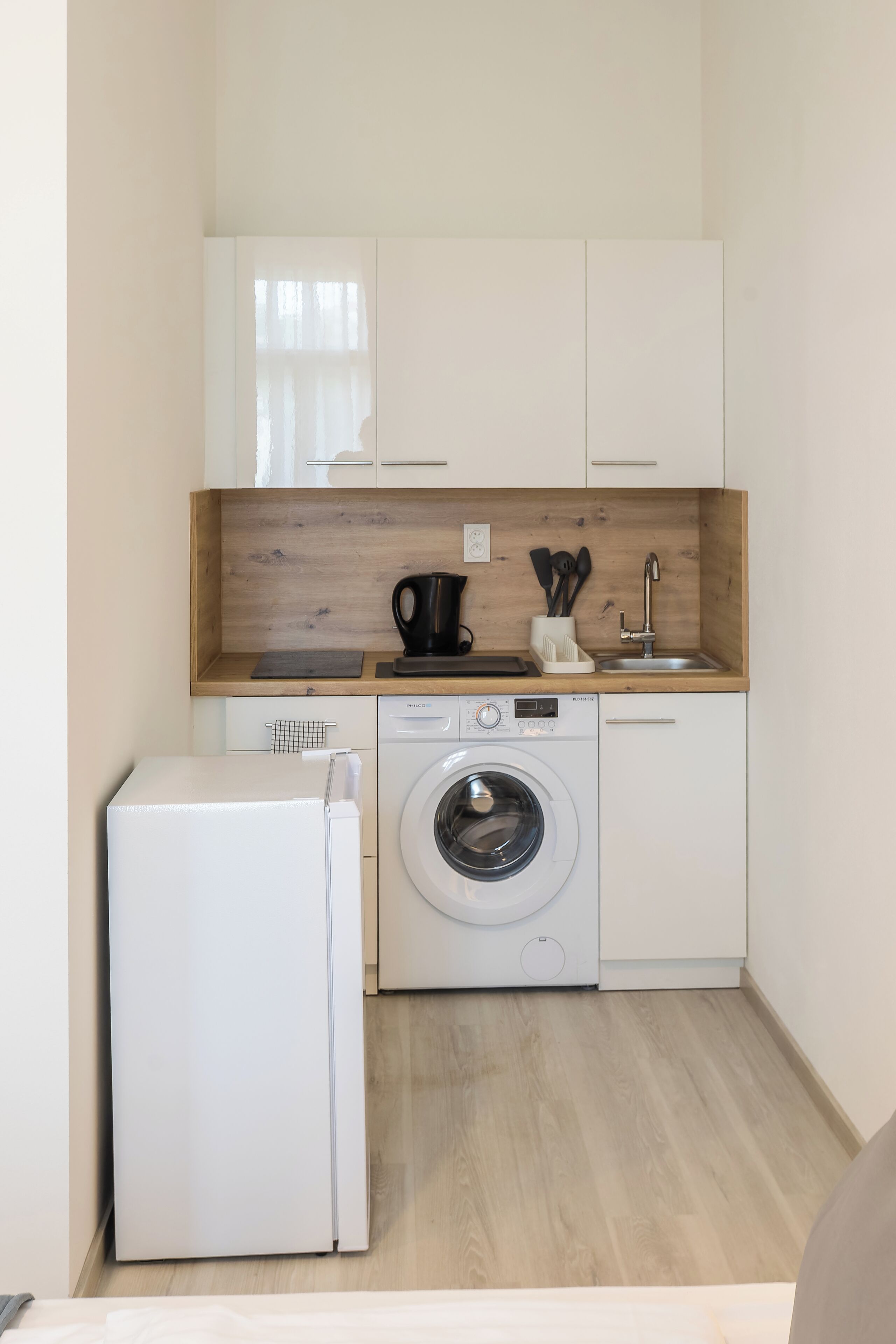 Eine kompakte Küche mit Waschmaschine, Kaffeemaschine und kleinem Kühlschrank.