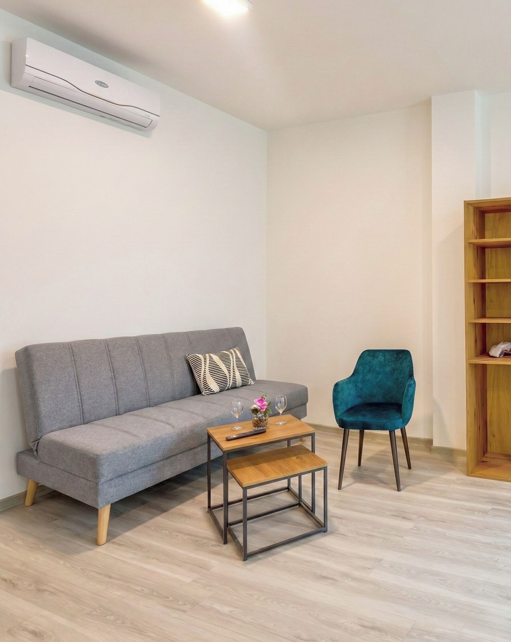 A modern living room with a grey sofa, a wooden coffee table, a teal armchair, and a wooden bookshelf.